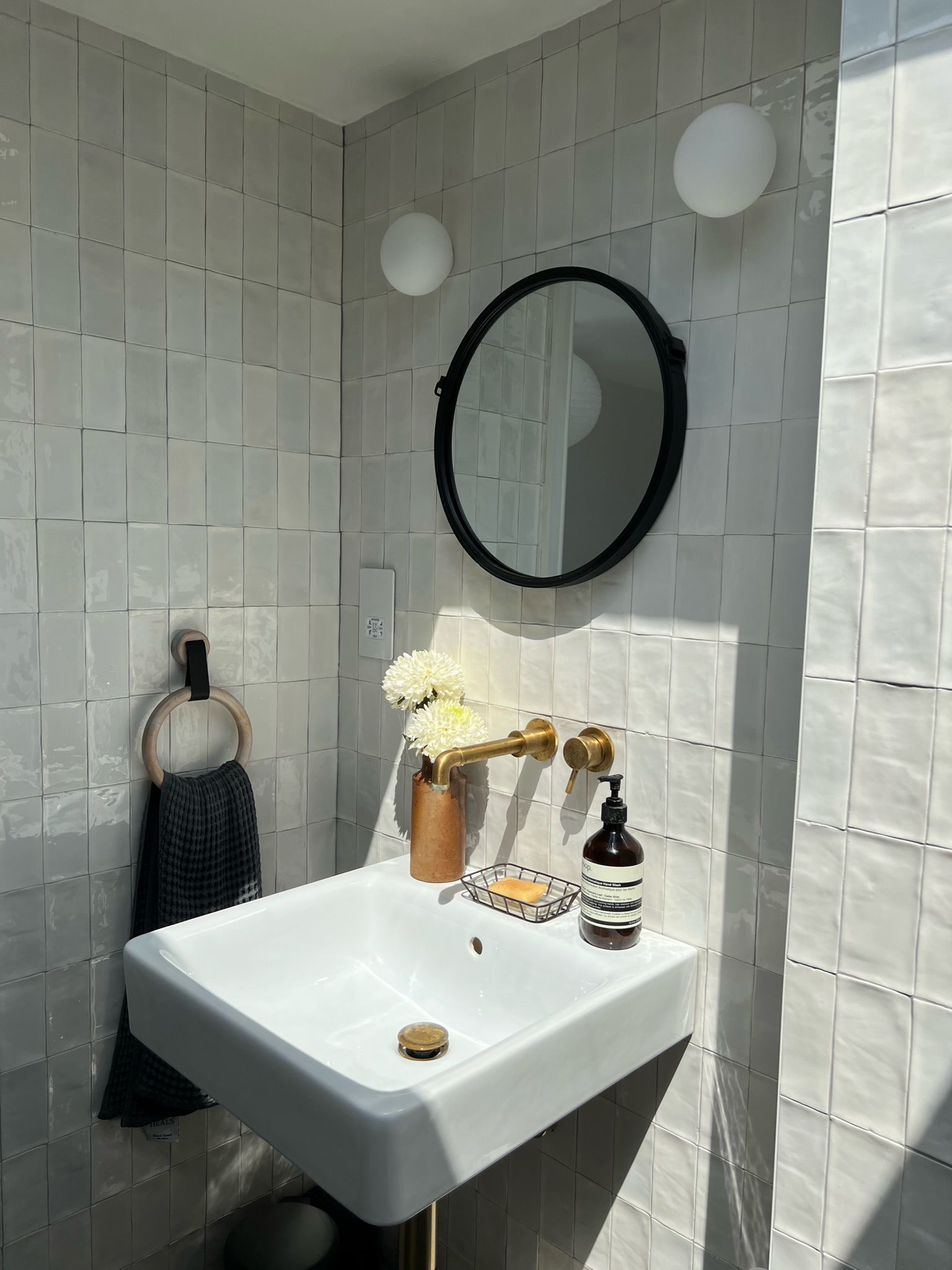Wall hung basin with brushed brass tap and round black mirror on handmade look tiles, W7