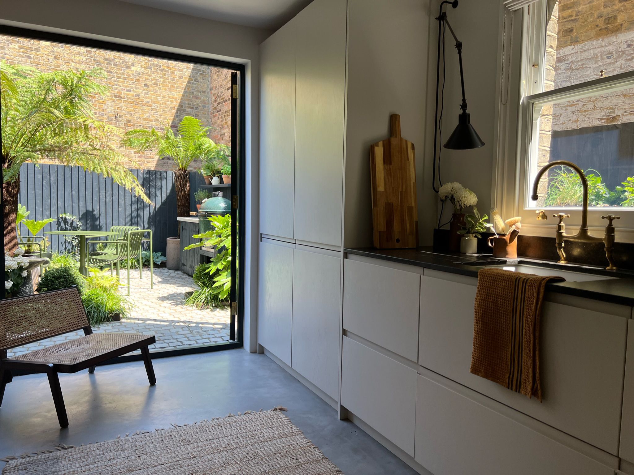 Kitchen with black framed glazed door opening onto a planted garden, Clairville Gardens W7