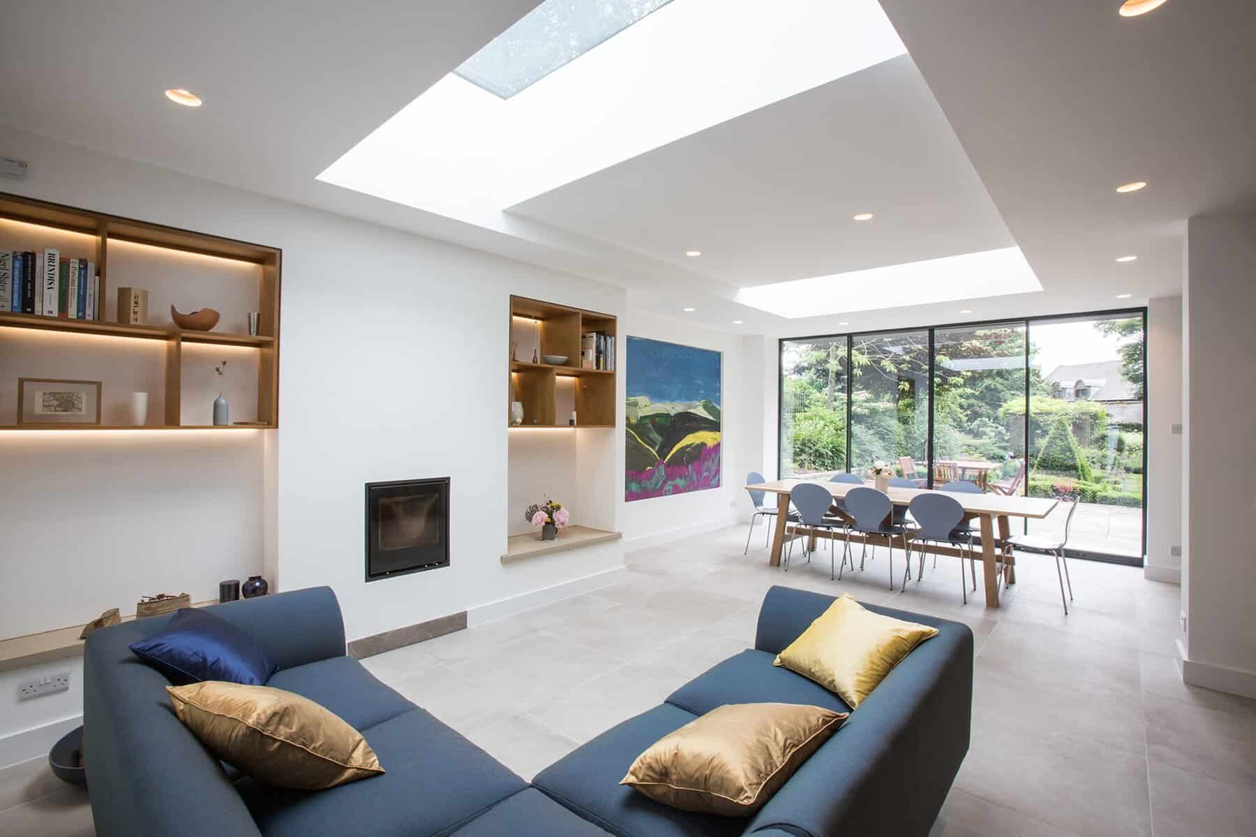 Living area with fitted lit shelving, roof lights and dining table by sliding doors, N5 extension