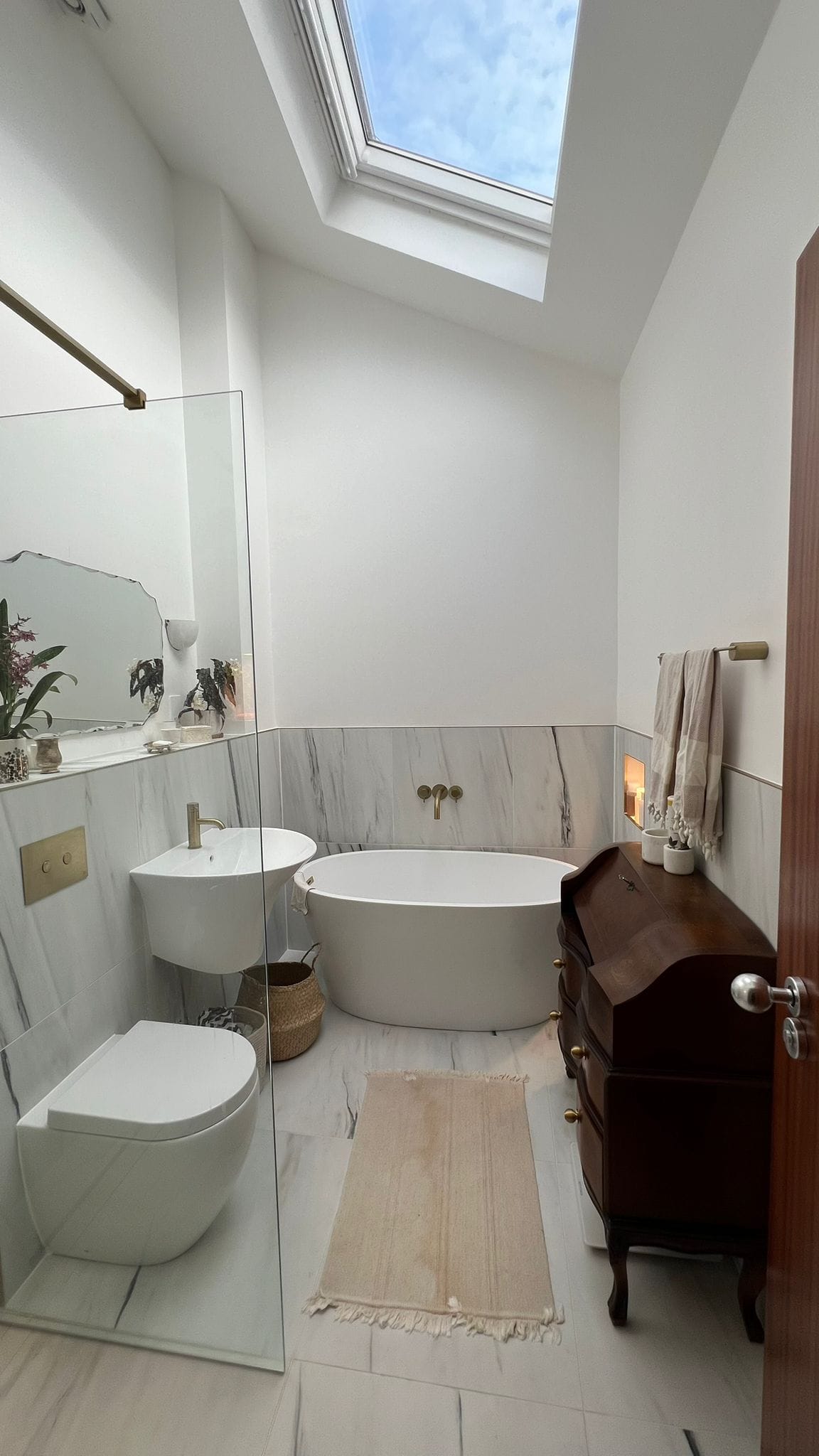 Bathroom with freestanding bath under a roof window, wall hung WC and marble effect tiling, Bow E3