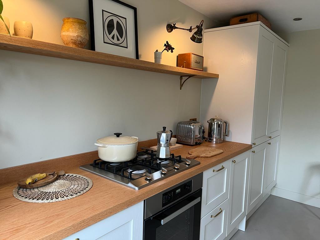Gas hob and built in oven below a floating oak shelf with black wall lights, tall ivory shaker units, W7